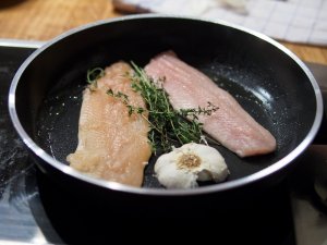 Saiblings- und Forellenfilet Ein Saiblings- und ein Forellenfilet, Thymian, und eine halbe Knoblauchknolle werden in einer Pfanne gebraten