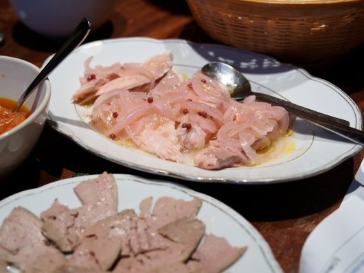 Marinierter Saibling und dünn aufgeschnittene Lammleber Marinierter Saibling mit rosa Beeren und Zwiebeln, im Vordergrund dünn aufgeschnittene Lammleber