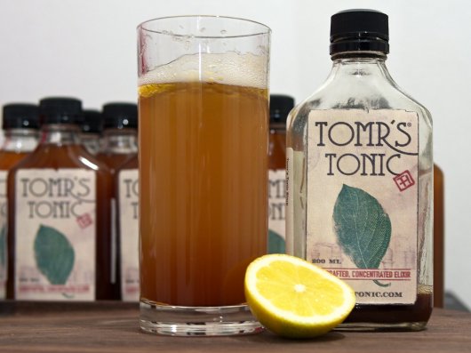 Ein fast leere Flasche "Tomr's Tonic"-Sirup, eine halbe Zitrone und ein Glas Tonic