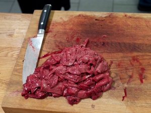 Rohe Kalbsleber In feine Scheiben geschnittene rohe Kalbsleber auf einem Schneidbrett, daneben ein großes Küchenmesser