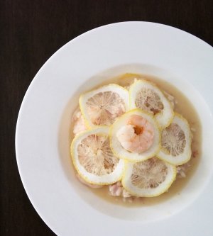 Risotto ai gamberi e cedri (am Tisch) Ein Teller mit Risotto ai gamberi e cedri, bedeckt von Zitronenscheiben und gekrönt mit einer Garnele