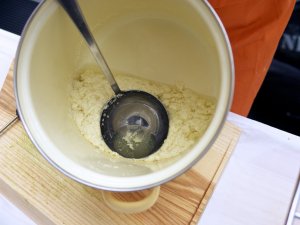 Flüssigkeit abschöpfen beim Tofu-Machen Mit einem großen Schöpflöffel wird die übrige Flüssigkeit ("Molke") nach der Gerinnung der Sojaproteine abgeschöpft