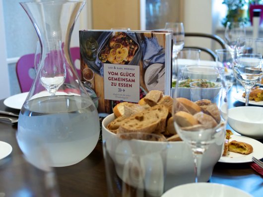 Ein festlich gedeckter Tisch mit dem Buch "Vom Glück gemeinsam zu essen" von Leo & Karl Wrenkh